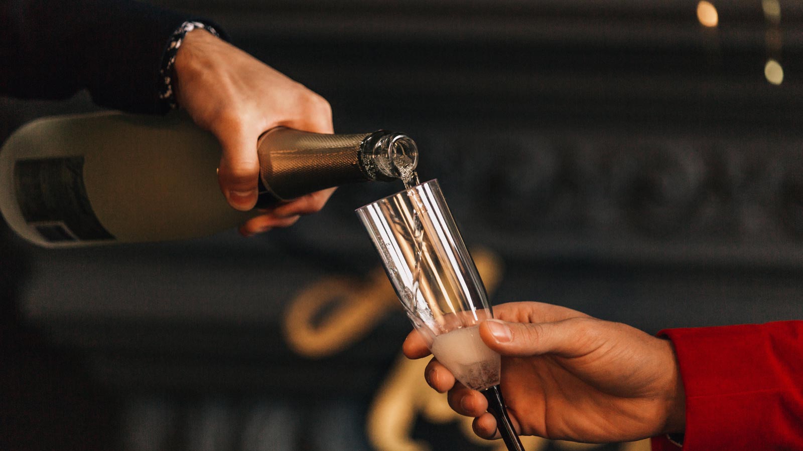 A person pouring champagne from a liquor bottle into a flute for another person